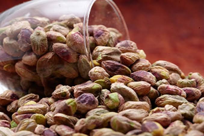 Pistachios in their shells spilling from a glass